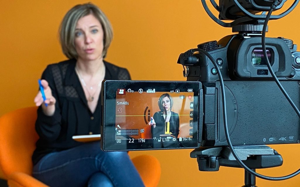Sacheen Sierro assise dans un fauteuil orange face à une caméra qui la filme symbolisant l'enregistrement des formations Sémantisseo ou d'études de cas sur la gamme de services.